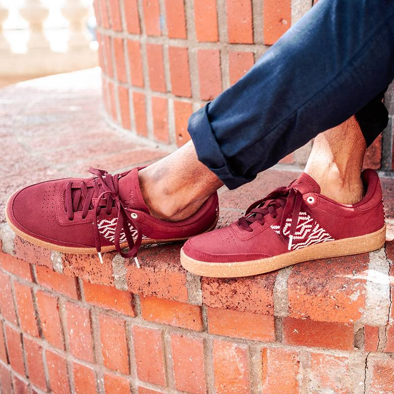 Baskets en daim rouge portées avec tissage rouge ethnique artisanal sur fond blanc. Saigon Suede Burgundy.