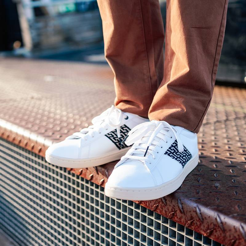 Modèle portant une paire de baskets en cuir avec des motifs ethniques artisanaux, lookbook. Ho Tay Classique Black.