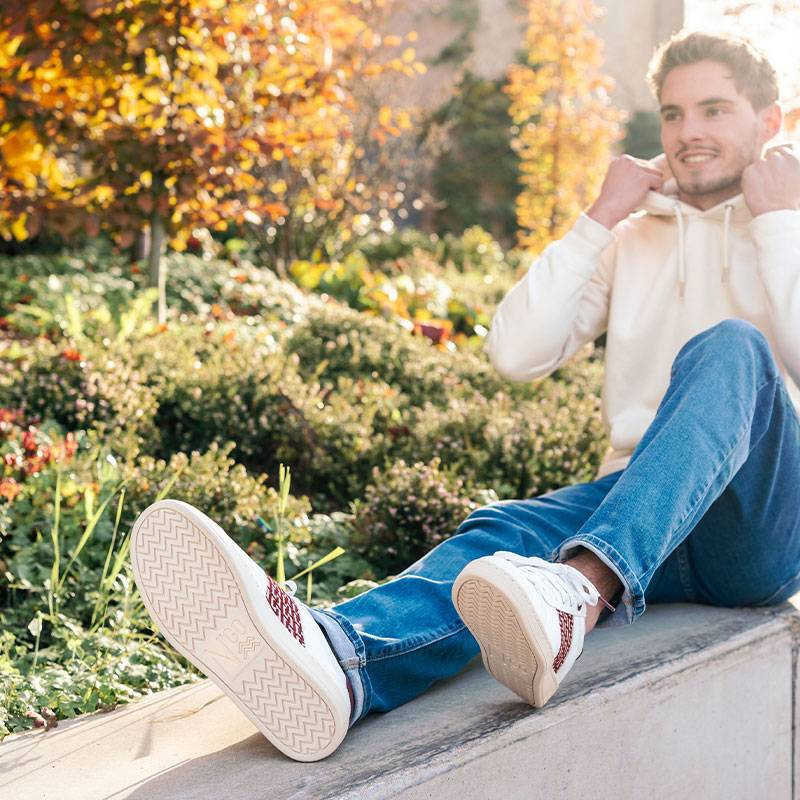 Modèle portant une paire de baskets en cuir avec des motifs ethniques artisanaux, lookbook. Ho Tay Burgundy.