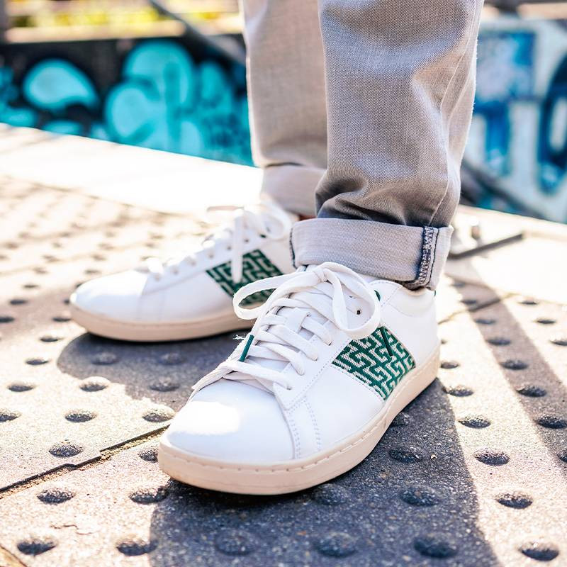 Modèle portant une paire de baskets en cuir avec des motifs ethniques artisanaux, lookbook. Ho Tay Classique Green.