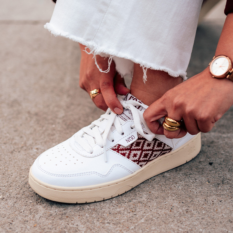 Modèle portant une paire de baskets en cuir avec des motifs ethniques artisanaux, lookbook. Hue Classique Burgundy.