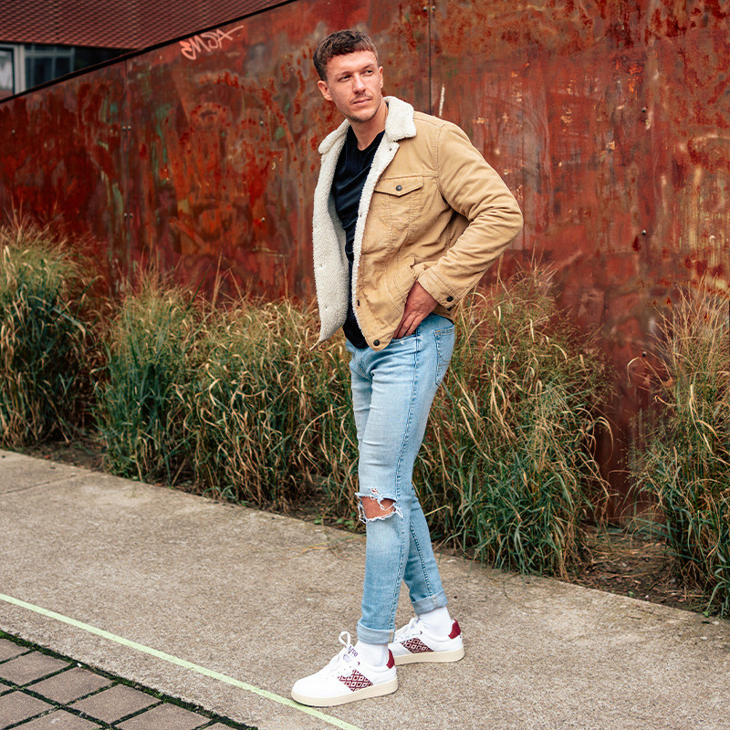 Modèle portant une paire de baskets en cuir avec des motifs ethniques artisanaux, lookbook. Hue Classique Burgundy.