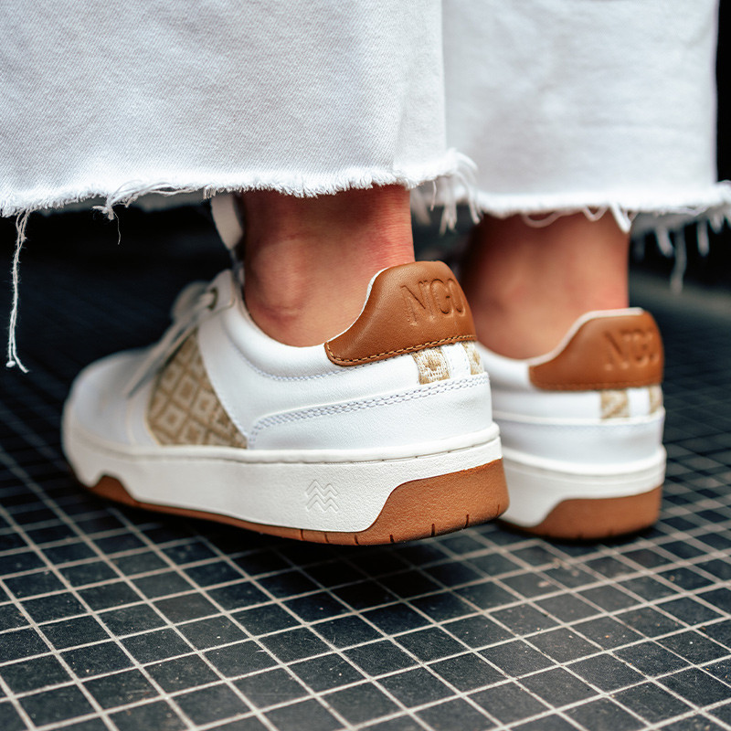 Modèle portant une paire de baskets en cuir avec des motifs ethniques artisanaux, lookbook. Hue Classique Sand Cognac.