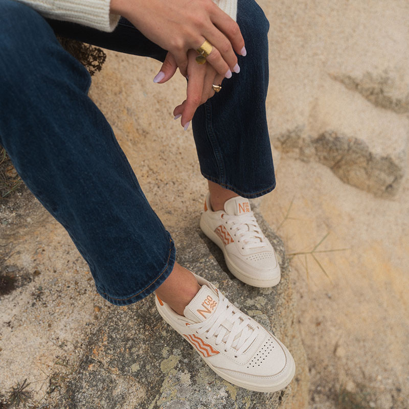 Femme portant une paire de baskets en cuir avec des motifs ethniques artisanaux, lookbook. Saigon Classique '24 Apricot.