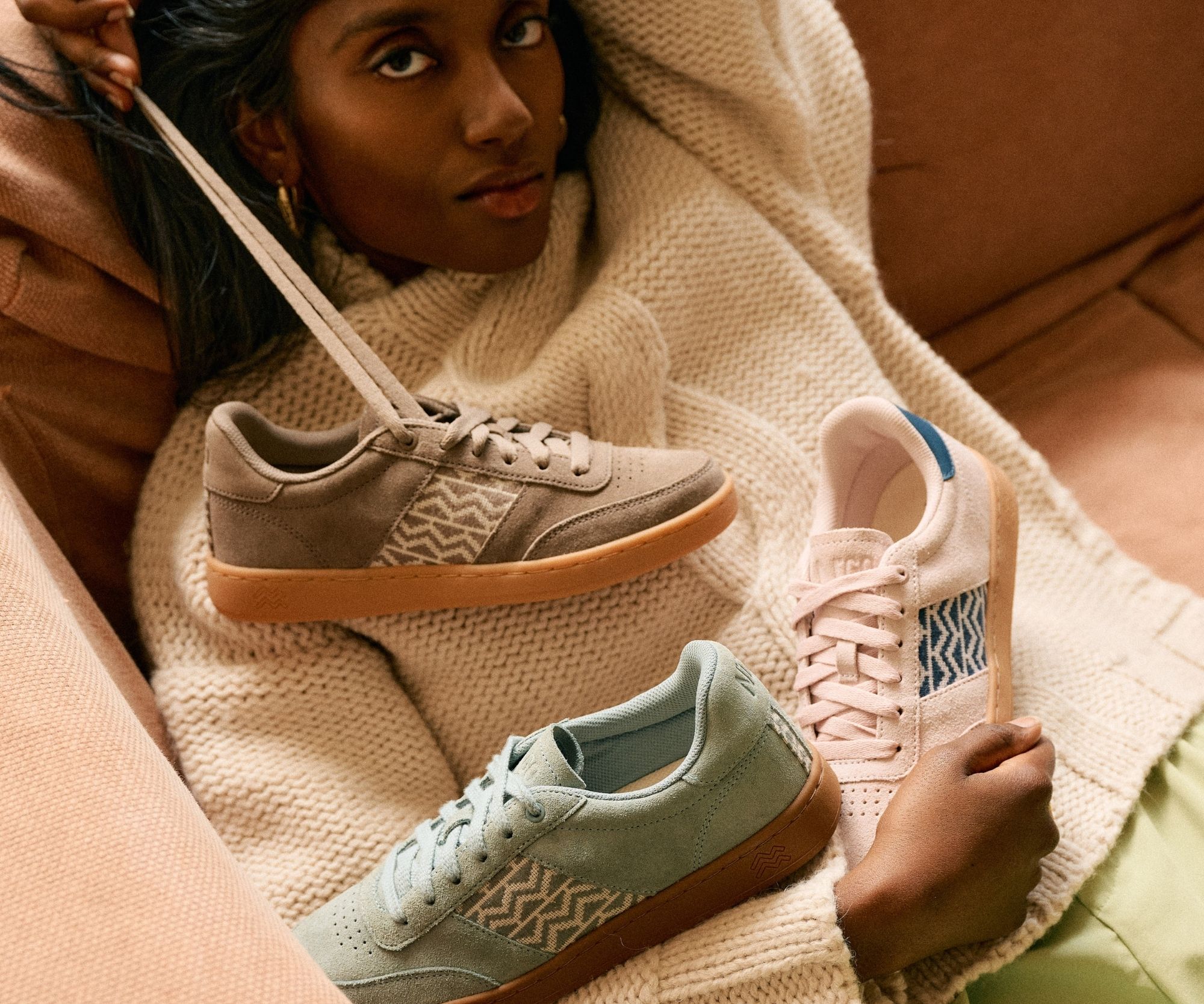 Des sneakers éco-responsables en matières naturelles suspendues au plafond par leurs lacets, créant une installation aérienne sous une charpente en bois rustique. Ces baskets durables, fabriquées avec du tissu tissé artisanal et du cuir vegan, sont dispon